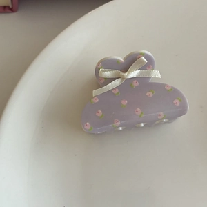 Detailed close-up of a lilac floral hair claw clip with a cream ribbon bow on white tray