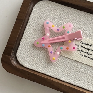 Detail shot of a pink star hair clip with colorful dots on a rustic linen background