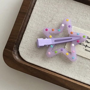 Close-up of a purple star hair clip with colorful polka dots on a wooden tray
