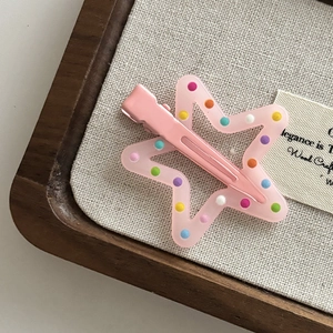 Detail of pink star hair clip with colorful polka dots and hollow design on a wood tray