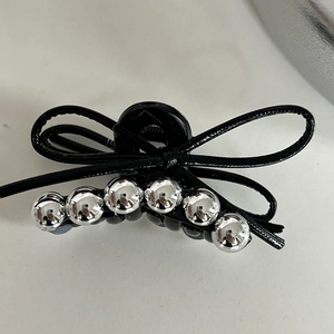 Close-up of black ribbon-shaped hair claw clip with silver bead accents on marble surface