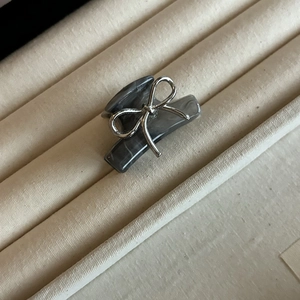 Close-up of a silver bow and dark gray marble texture hair claw clip on a beige tray