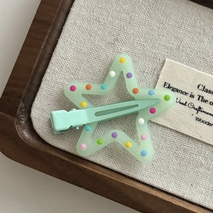 Close-up of star-shaped hair clip with colorful dots on a natural linen background