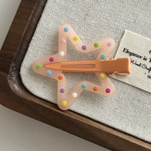 Close-up of a pink star hair clip with colorful polka dots and orange metal base