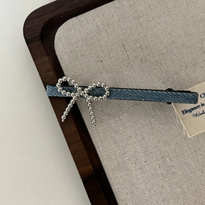 Barrette en denim bleu avec nœud en perles argentées sur une surface en lin