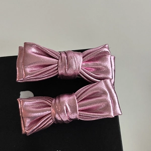 Close-up of two pink metallic bow hair clips with lustrous fabric texture details