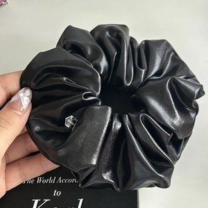 Glossy black scrunchie with metallic finish and silver charm on white background
