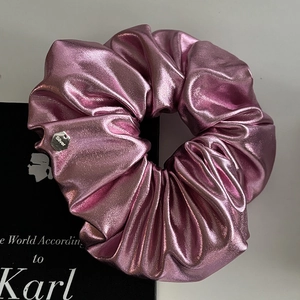Detail of pink metallic scrunchie with shiny texture and silver tag on a book