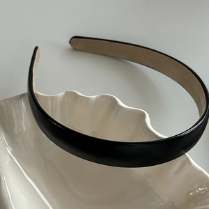 Détail d'un serre-tête minimaliste en similicuir noir sur un plateau en céramique