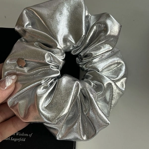 Detail of silver metallic fabric scrunchie with pleated texture and small hexagon metal tag