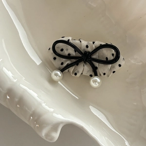 Polka dot bow hair clip with black metal frame and elegant faux pearls on a shell tray