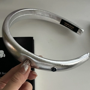 Detail of silver metallic padded headband featuring a hexagonal metal tag and handmade label