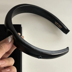 Detail of hand-made wide black leather headband with hexagon metal tag and gold lettering