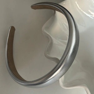 Gros plan d'un serre-tête en métal argenté mat posé sur une assiette décorative blanche