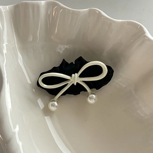 Detailed view of a black ruffled bow hair clip with faux pearls on white shell tray
