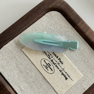 Detail of glitter resin hair clip with light green and purple gradient in a wooden box