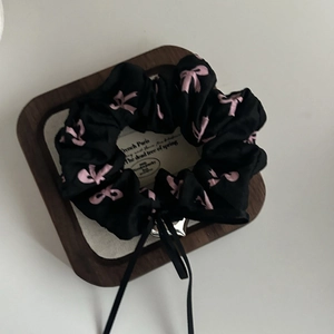 Detail of black satin scrunchie with pink bow patterns and long ribbons on a wooden tray