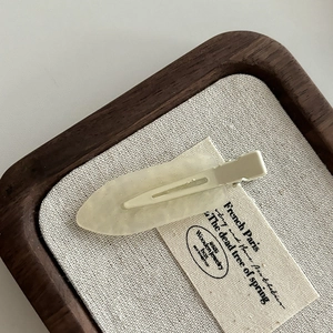 Close-up of a leaf-shaped matte cream hair clip on a natural linen and wooden display tray