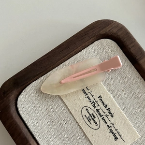 Close-up of translucent resin hair clip with pink metal clip on a beige linen base