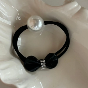 Elegant black hair tie with large white pearl and rhinestone bow on a shell tray
