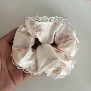 Gros plan d'un chouchou en satin fleuri avec motifs roses et bordure en dentelle