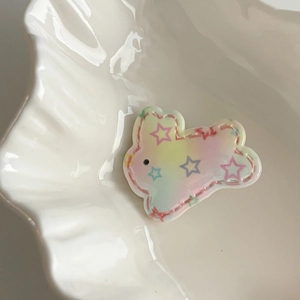 Cute rainbow gradient bunny hair clip with star patterns on a white shell tray