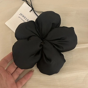 Détail d'un grand chouchou fleur en satin noir avec une texture brillante et étiquette