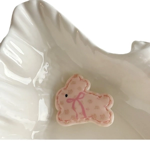 Pink rabbit hair clip with floral patterns and ribbon in a white shell dish