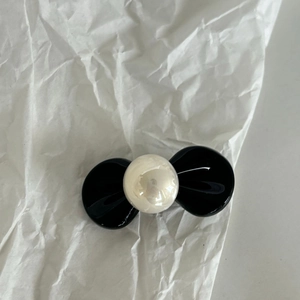 Fermaglio per capelli a fiocco nero con perla bianca sintetica su sfondo di carta bianca