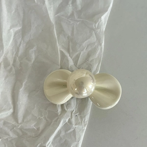 Dettaglio del fermaglio a fiocco color crema con perla centrale su sfondo bianco