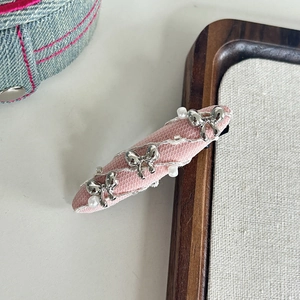 Détail d'une pince à cheveux en résille rose avec nœuds argentés et perles nacrées