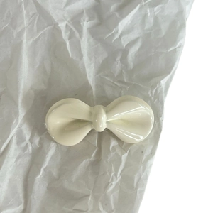 Graziosa clip per capelli a fiocco color crema su sfondo di carta strutturata