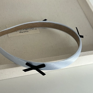 Detail of light blue satin headband with black bows on a cream display tray