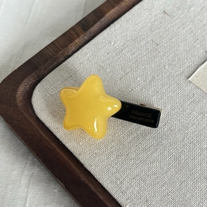 Handmade yellow star-shaped acetate hair clip on a wooden tray for women