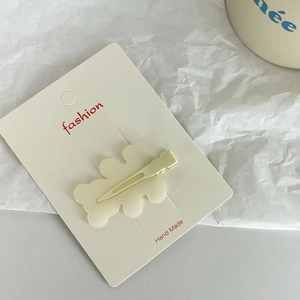 Close-up of cream-colored wavy duckbill hair clip on card with aesthetic background