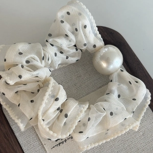 Detailed view of polka dot mesh scrunchie featuring a large pearl on wooden tray