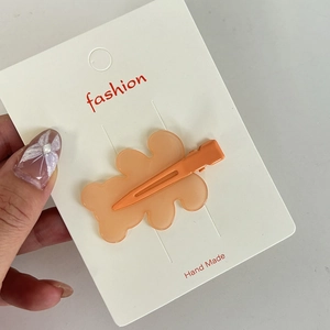 Detail shot of a matte orange wavy resin hair clip with matching color metal duckbill clip