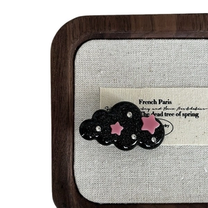 Sparkly black cloud hair clip with pink star accents and crystals on linen backdrop