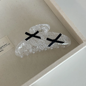 Detail of transparent lace hair claw with black bows on a beige display tray