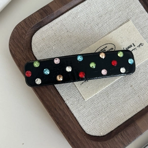 Detailed macro view of black rectangular hair clip with colorful rhinestones on beige fabric