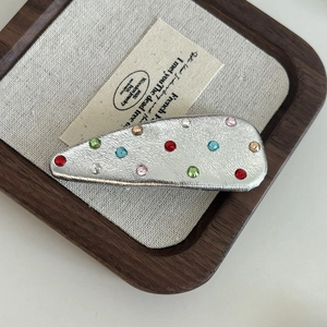 Close-up of silver leather teardrop hair clip with multicolored rhinestones in tray
