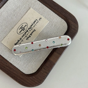 Detail of silver faux leather hair clip with colorful rhinestones on a wooden tray