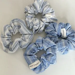 Close-up of four blue striped knitted scrunchies with white labels on a gray background