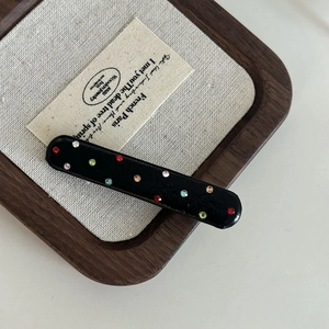 Detail of a black leather hair clip with colorful rhinestones on a burlap card