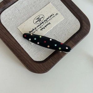Close-up of a black hair clip with colorful rhinestones on a wooden tray