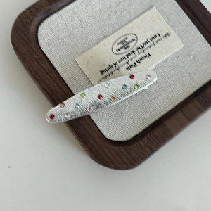 Macro shot of silver brushed alloy hair clip with multicolored rhinestones on tray