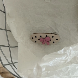 Close-up of a beige polka dot hair clip with a pink bow on a textured white surface