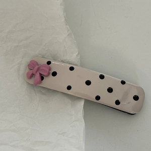 Detail of pink bow hair clip with black polka dots on a cream rectangular base