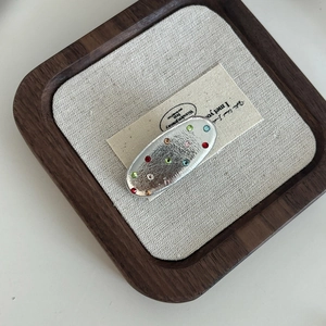 Macro shot of silver leather-textured oval hair clip with colorful rhinestones on wood