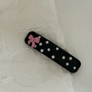 Close-up of pink bow and white polka dots on a glossy black hair clip detail